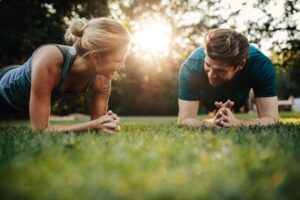 Fit young man and woman exercising in park. Smiling caucasian couple doing core workout on grass.